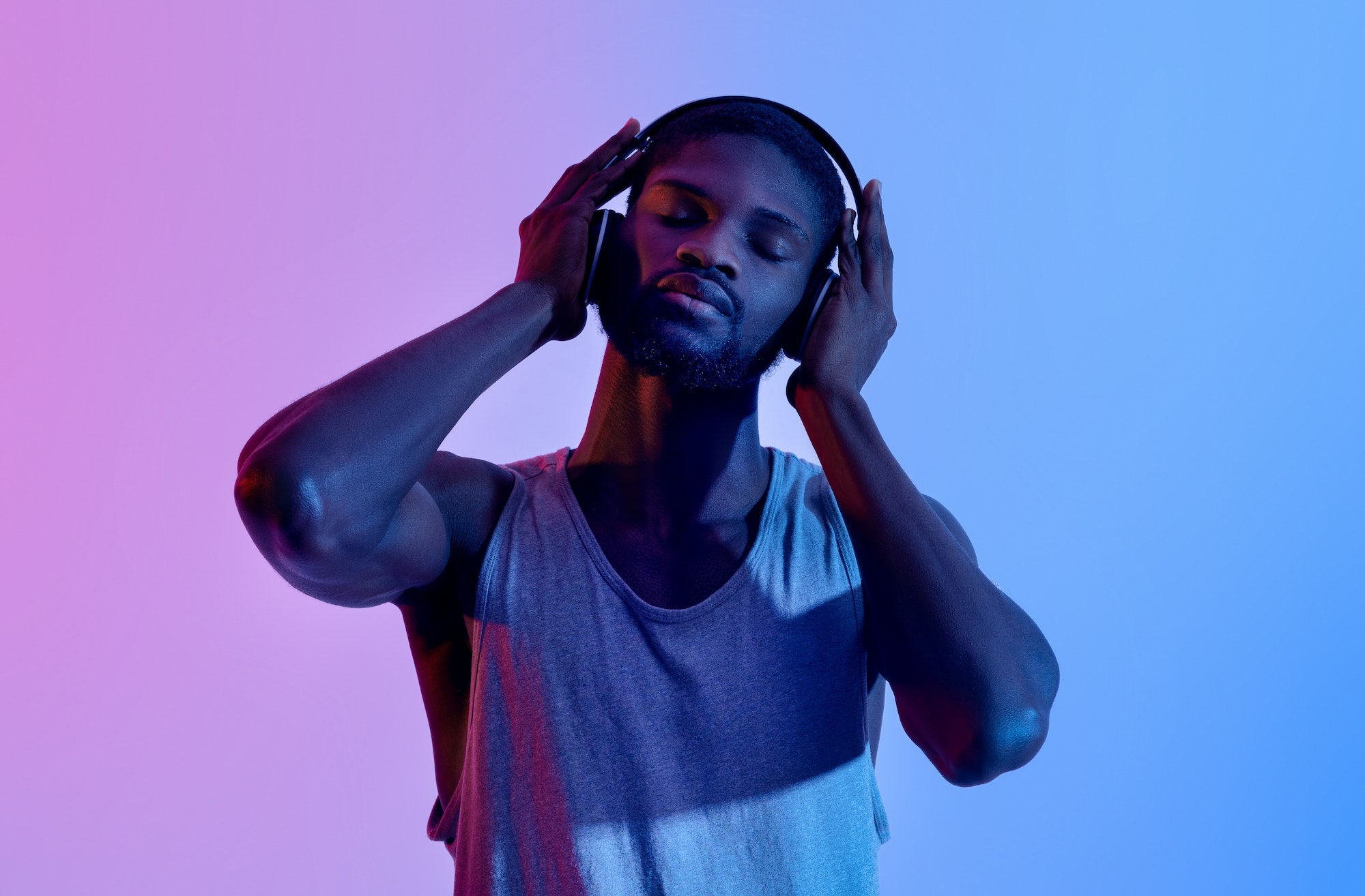 Peaceful black athlete listening to music in headphones on break from his training in neon light