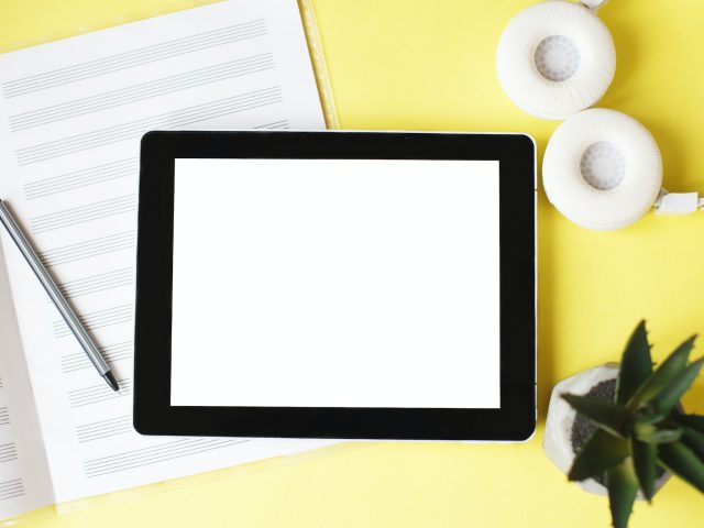 Top view open music book, headphones and a pen on a yellow background. mock up for music lessons