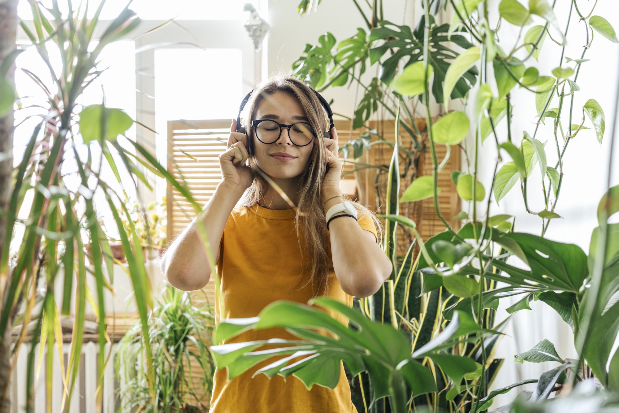 Young woman surrounded by plants listening to music with headphones